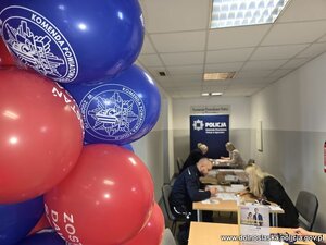 Kobiety siedzą za stołem , pobierany patyczkiem materiał genetyczny. Widać logo policji i fundacji DKMS