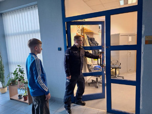 chłopiec wchodzi do komisariatu policji, wita go policjant, chłopiec przymierza stroje policyjne, robi sobie zdjęcia.