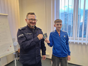 chłopiec wchodzi do komisariatu policji, wita go policjant, chłopiec przymierza stroje policyjne, robi sobie zdjęcia.