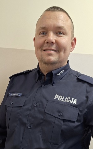 policjant uśmiechnięty, stoi a tle ściany.