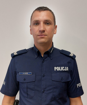 policjant stoi na tle białej ściany i pozuje do zdjęcia.