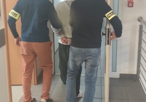 złota biżuteria. monety, kosztowności leżą na stole. Policjanci prowadzą zatrzyamanego.