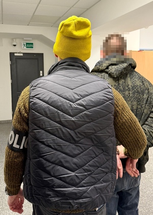 Policjant prowadzi zatrzymanego - widok z tyłu.