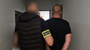 Mężczyzna oddaje odciski palców. Prowadzony jest przez policjantów.