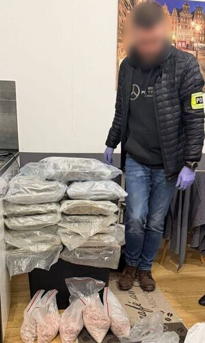 policjant stoi, przed nim leżą narkotyki w workach.