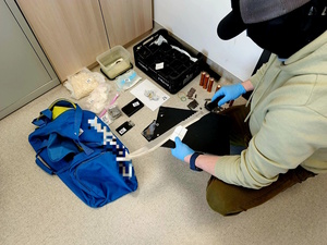 narkotyki leżą na podłodze. Policjant sprawdza i ogląda zawartość.