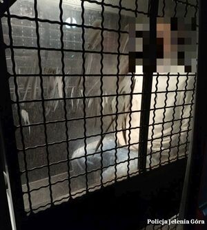 Zatrzymany siedzi w pomieszczeniu kratami.