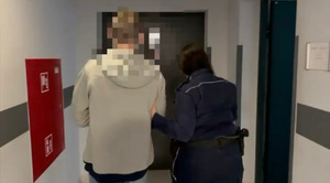 Policjantka prowadzi korytarzem zatrzymanego mężczyznę.