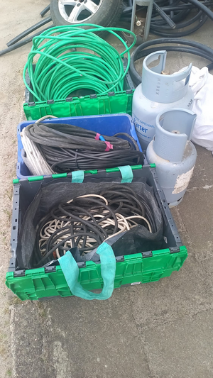 Policjanci prowadzą zatrzymanych. Kable porozkładane na ziemi w pudełkach i kartonach.