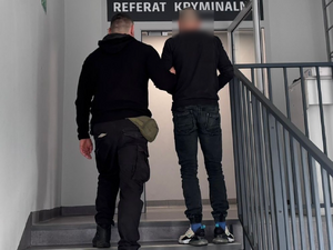 Policjanci prowadzą zatrzymanych. Kable porozkładane na ziemi w pudełkach i kartonach.