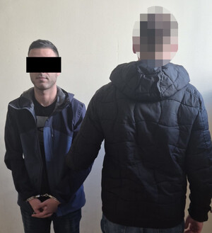 Policjant z zatrzymanym mężczyzną zakutym w kajdanki.