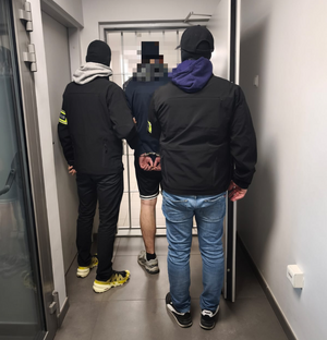 Dwaj policjanci z zatrzymanym na korytarzu.