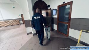 Policjant z zatrzymanym mężczyzna zakutym w kajdanki.