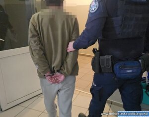 Policjant z zatrzymanym mężczyzna zakutym w kajdanki.