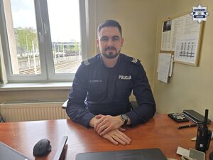 Umundurowany dzielnicowy siedzi za biurkiem.