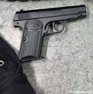 policjanci prowadzą zatrzymanego,  pistolet lezy na stole.