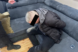 Siedzący na kanapie zatrzymany mężczyzna.