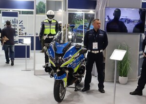 Zdjęcie przedstawia motocykl policyjny oraz stojącego przy nim funkcjonariusza Policji