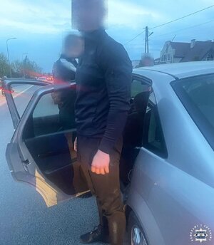 Zatrzymany mężczyzna stoi przy samochodzie osobowym, który ma otwarte drzwi od strony kierowcy.