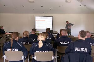 Uczestnicy szkolenia siedzą na sali. W tle widoczna jest osoba, która prowadzi szkolenie.