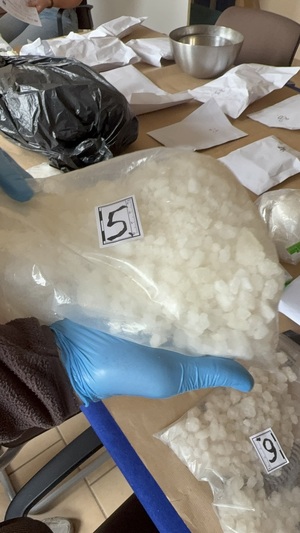 policjanci prowadza zatrzymanego, Na stole w workach plastikowych porozkładane marihuana, kryształ.