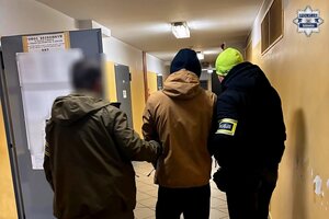 Dwaj funkcjonariusze z zatrzymanym na korytarzu.