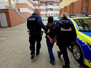 Policjant i policjantka prowadzi zatrzymanego mężczyznę obok radiowozu.