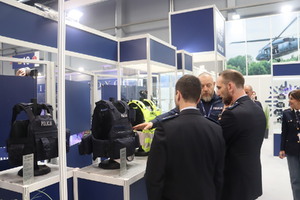 Zdjęcie przedstawia eksperta z obszaru uzbrojenia i techniki policji, przedstawiającego zainteresowanym nowoczesne kamizelki kuloodporne dedykowane policjantom komórek patrolowo-interwencyjnych oraz ruchu drogowego