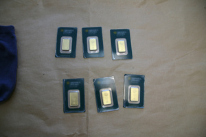 Pieniądze porozkładane na stole. Widać złote sztabki, łańcuszki, pierścionki i pieniądze w tym dolary, euro.