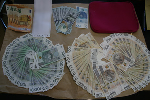 Pieniądze porozkładane na stole. Widać złote sztabki, łańcuszki, pierścionki i pieniądze w tym dolary, euro.