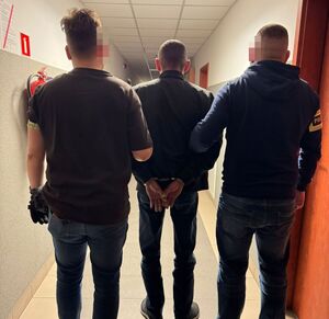 Dwaj funkcjonariusze na korytarzu z zatrzymanym mężczyzną.