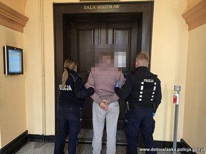 policja prowadzi zatrzymanego mężczyznę, widać napis na plakietce policja.