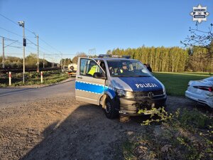 Policjant stoi przy radiowozie na miejscu zdarzenia przy przejeździe kolejowym.