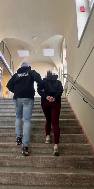 Policjant prowadzi zatrzymaną po schodach.