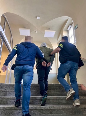 Policjanci prowadzą zatrzymanego po schodach.