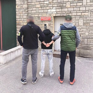 Policjanci trzymają zatrzymanych w kajdankach