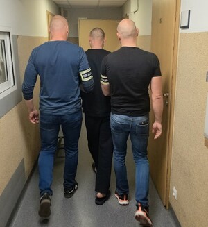 Dwaj policjanci prowadza zatrzymanego mężczyznę.