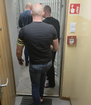 Dwaj policjanci prowadza zatrzymanego mężczyznę.