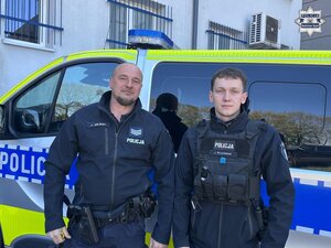 Dwaj policjanci stoją przy radiowozie.