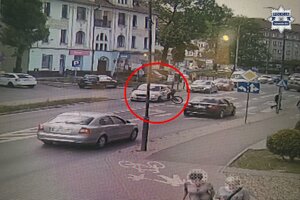 Fragment drogi, na której są osoby i pojazdy, a w czerwonym kółku zaznaczona została rowerzystka, przy pojeździe po uderzeniu w nie.