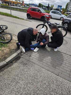 Policjant udziela pierwszej pomocy rowerzyście siedzącemu na ziemi obok roweru.