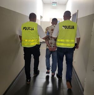 Policjanci prowadzą zatrzymanego mężczyznę korytarzem.