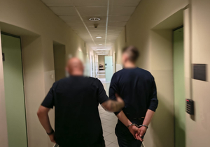Policjant prowadzi zatrzymanego korytarzem.