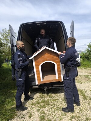 Policjanci trzymają budę dla psa.