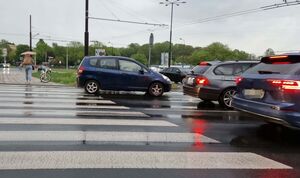 Auta na jezdni, jedno z nich tylnymi kołami stoi na przejściu dla pieszych.