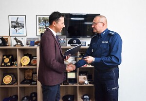 Komendant Centrum Szkolenia Policji w Legionowie insp. dr Rober Żółkiewski i Dyrektor Zarządzający Polską Platformą Bezpieczeństwa Wewnętrznego Rashel Talukder ściskają sobie dłonie i wymieniają się teczkami z podpisanym porozumieniem.