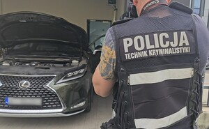 policjant stoi przed samochodem i robi mu zdjęcie.