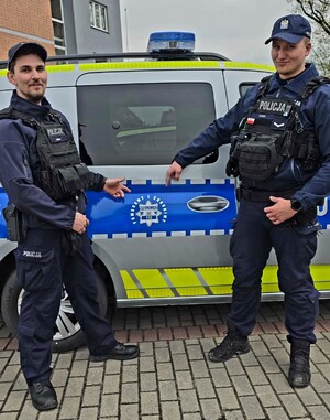 dwóch policjantów stoi przy radiowozie.