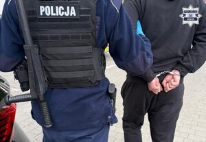 Policjant prowadzi osobę zatrzymaną.