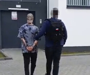 Policjant prowadzi zatrzymanego - widok z tyłu.